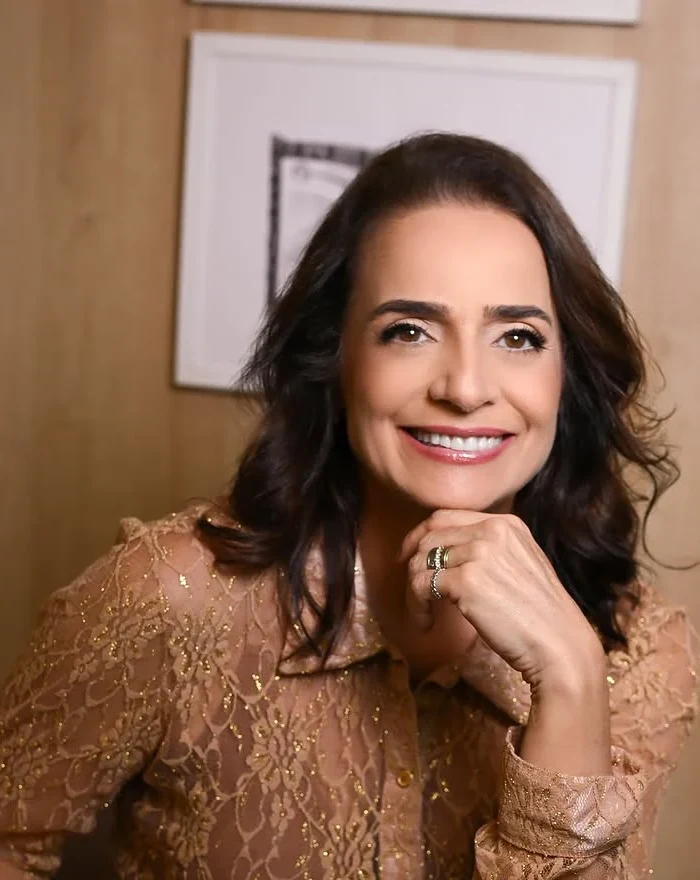 Dra. Luciana Maldonado sorrindo, com a mão no queixo, de blusa de renda caramelo